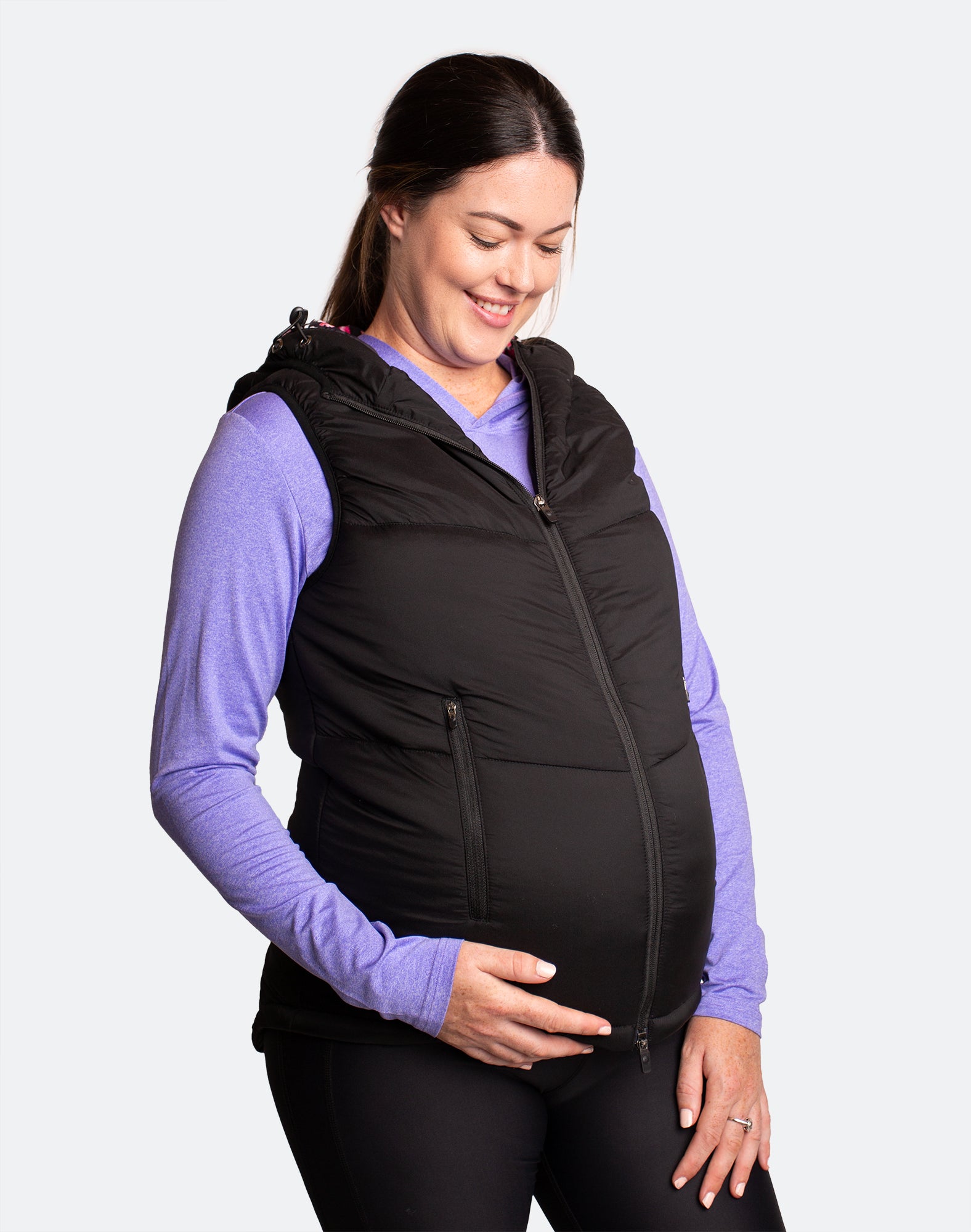 Happy mother wearing a black women&#39;s puffer vest over her maternity clothing